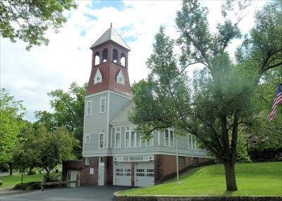 An old brick firehouse flanked by green trees and grass