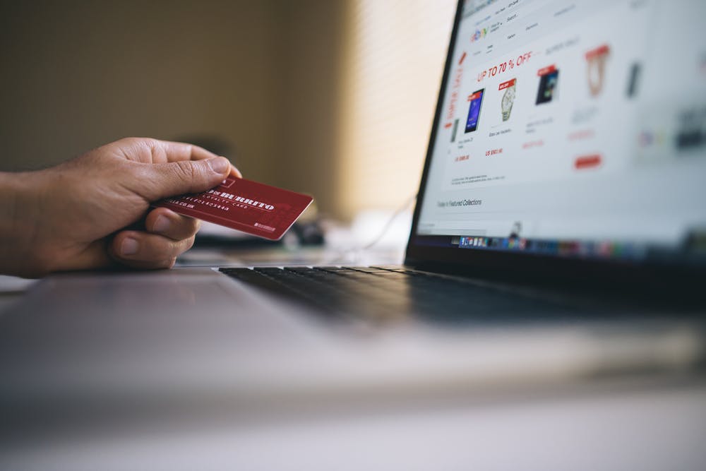 A hand holds a credit card in front of a computer to pay a bill 