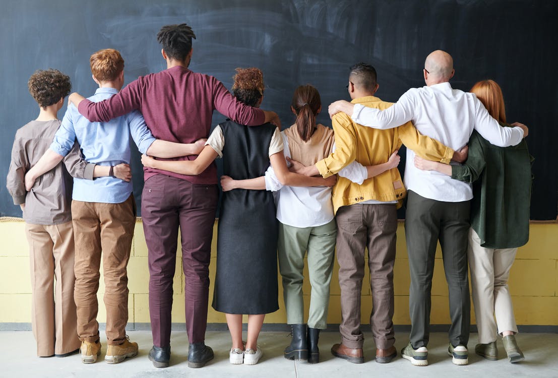 A group of people stand with their arms around each other and backs to the camera