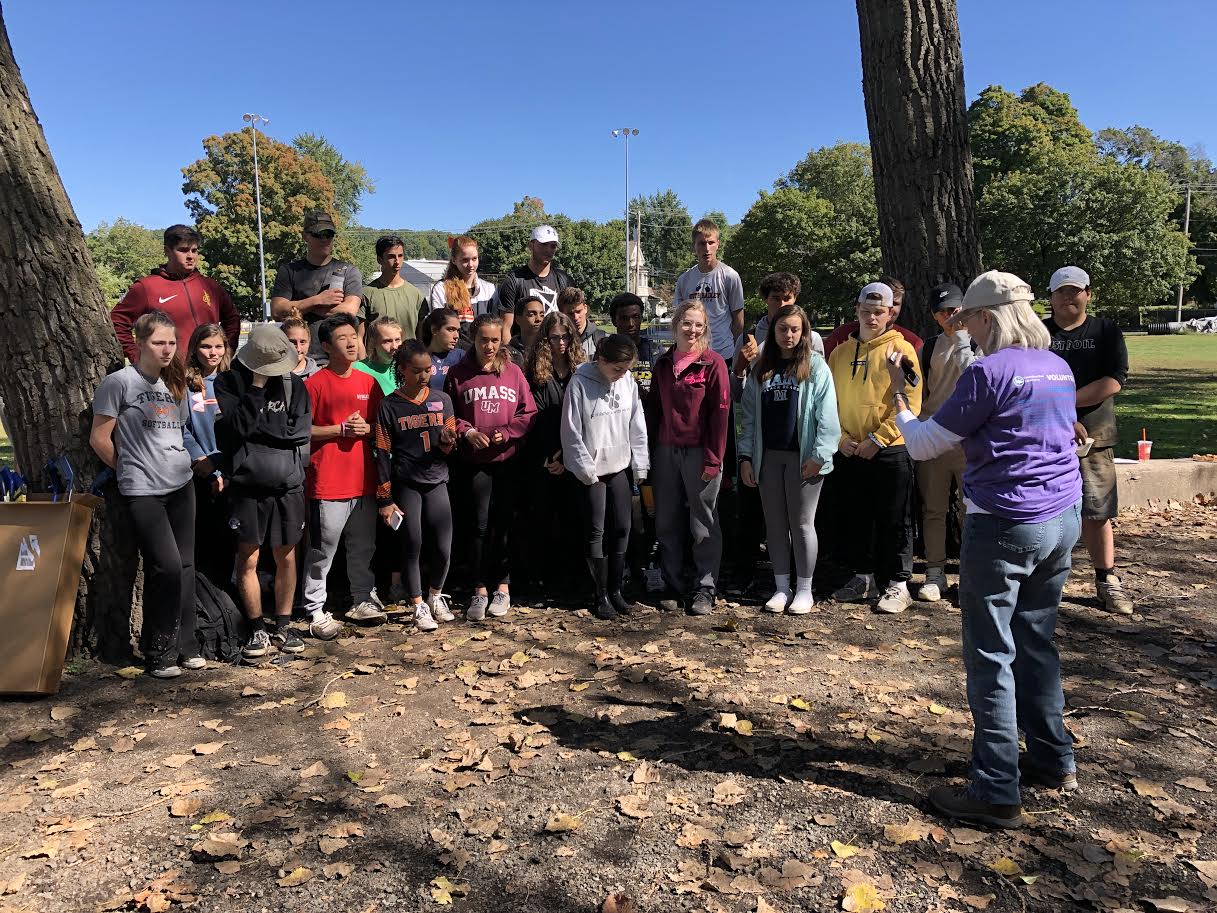 A woman thanks a group of students gathered in front of collected trash pulled from a river